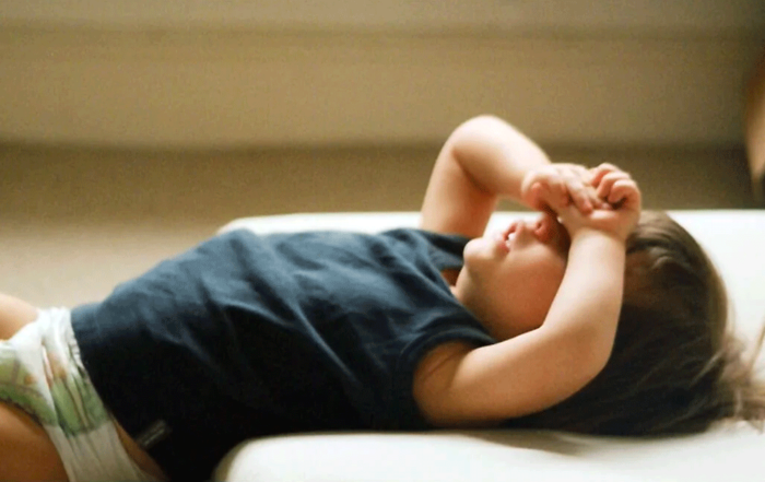 A toddler wearing diapers laying on his back with his arms across his face, having a tantrum.