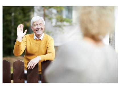 An older man waving at his neighbor outdoors on his porch.