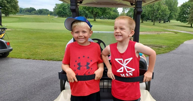 2 young boys riding on the back of a golf cart.