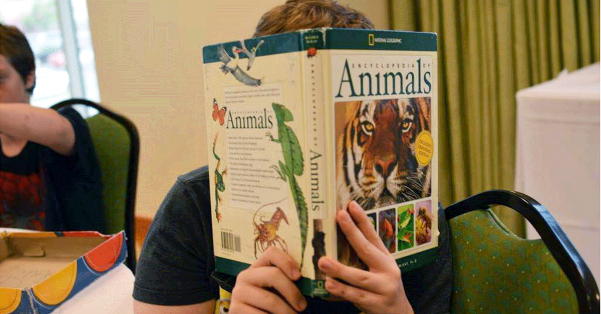 Young boy with Fragile X syndrome hiding behind a book.