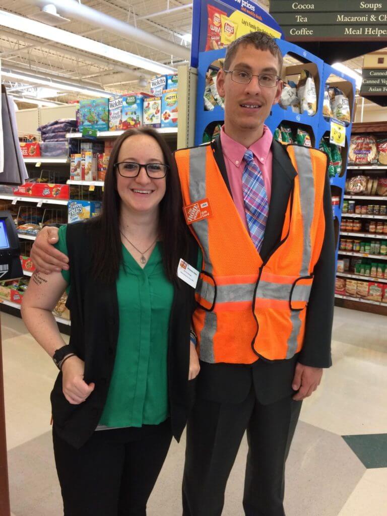 Ian, who has Fragile X syndrome, wearing a day-glow orange vest and standing next to a co-worker at Kroger's grocery store.