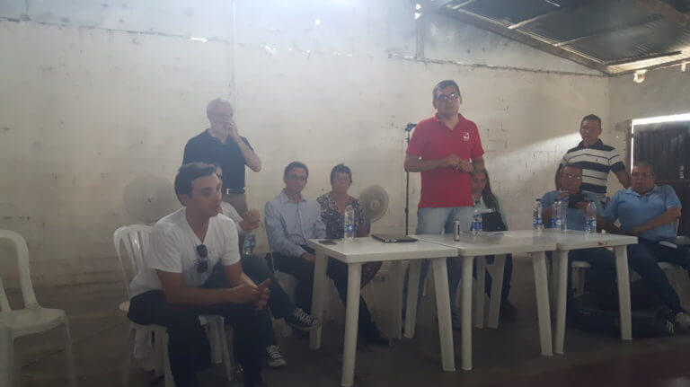 Several men, some sitting and some standing, in a sun-drenched room.