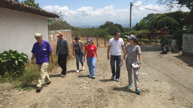 Several team members and local people walking along a dirt road next to a building.