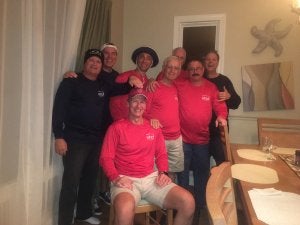 8 adults, one sitting, 4 with matching shirts, at a restaurant