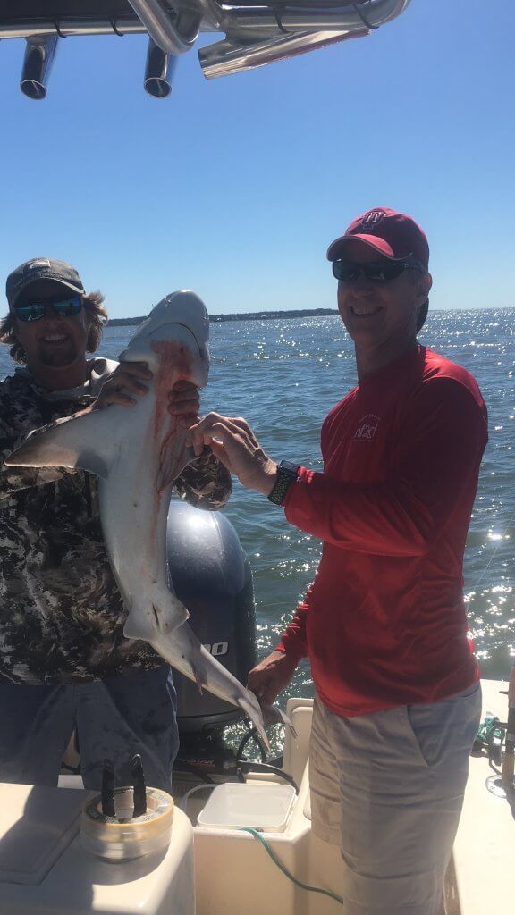 2 adult men on a boat holding up a shark