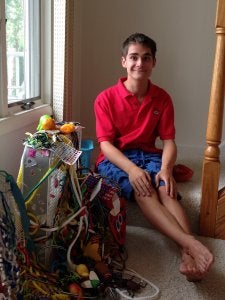 A barefoot teenage boy wearing a t-shirt and shorts, sitting in his bedroom next to a toy.