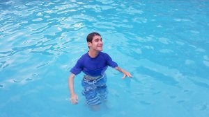 Teenage boy wearing a blue t-shirt and jeans standing in a swimming pool with water up to his waist