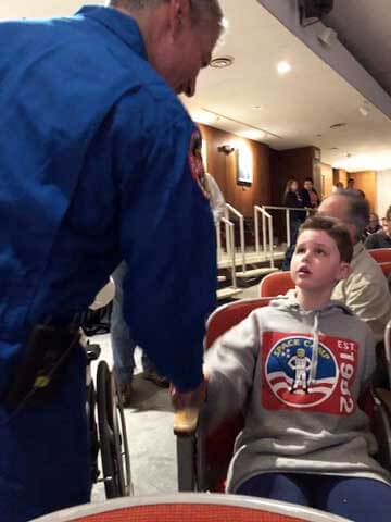 Riley, seated, shaking hands with astronaut Mark Vande Hei at space camp.