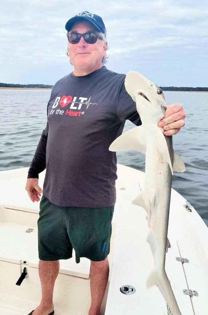 A fisherman on a boat on the water holding a 4 foot shark.