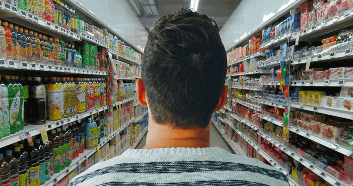 A young man facing a long aisle of groceries.