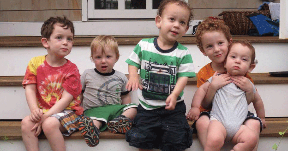 Four young boys and an infant on their front porch steps.