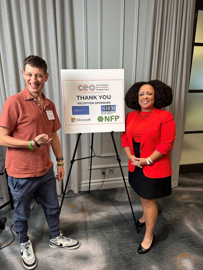 Dillon by a thank you sign posing with a fellow attendee.