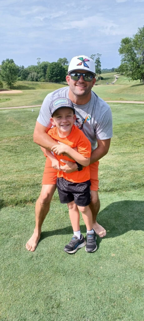 A barefoot dad playfully hugging his son on a golf course.