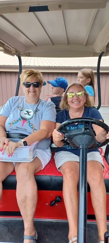Two women in the front seat of a golf cart, with two children in tow.