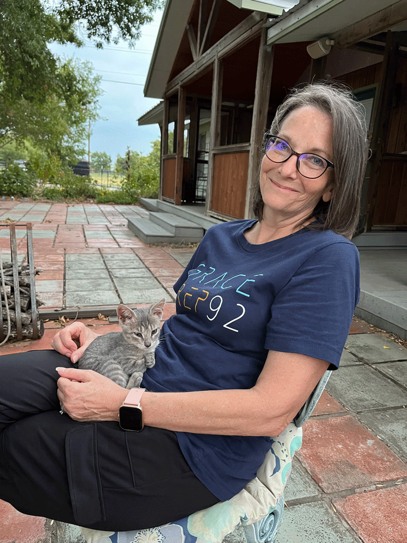 Donna Codd sitting and smiling on her patio petting a sweet kitten.