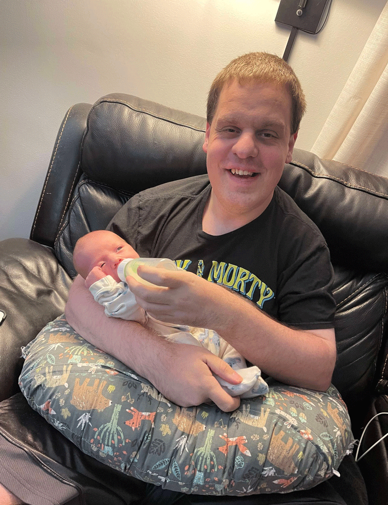 Philip Kemp feeding a tiny infant on his lap.