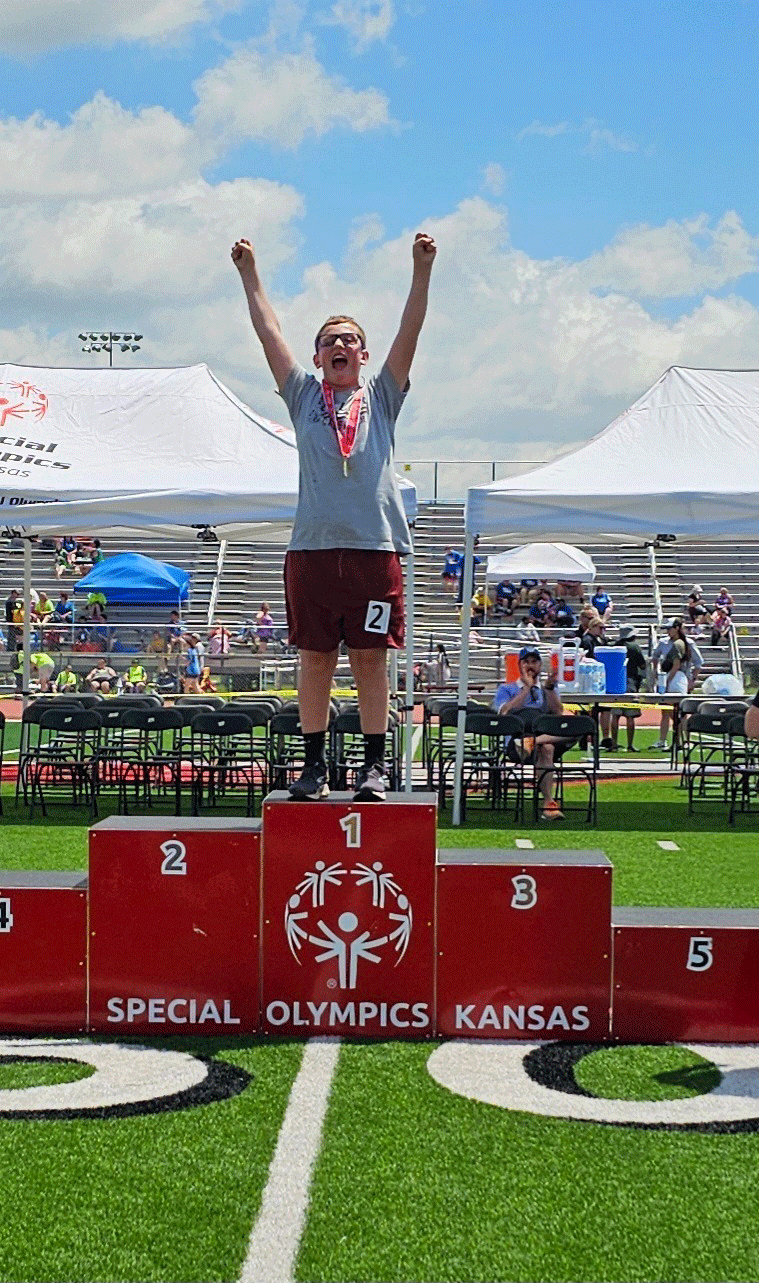 Owen Stauffacher standing on the Gold Medal stand with his arms raised in victory!