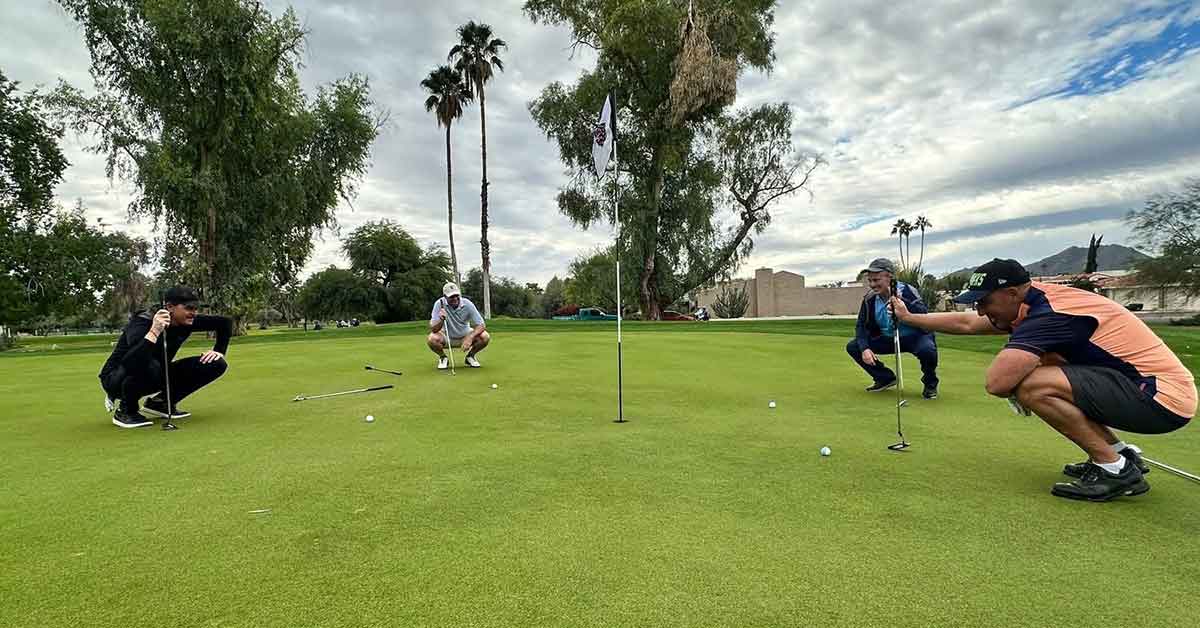 Golfers kneeling around the hole planning out out their next shot.