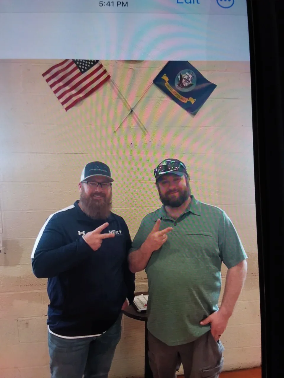 Two men smiling giving the peace sign underneath flags