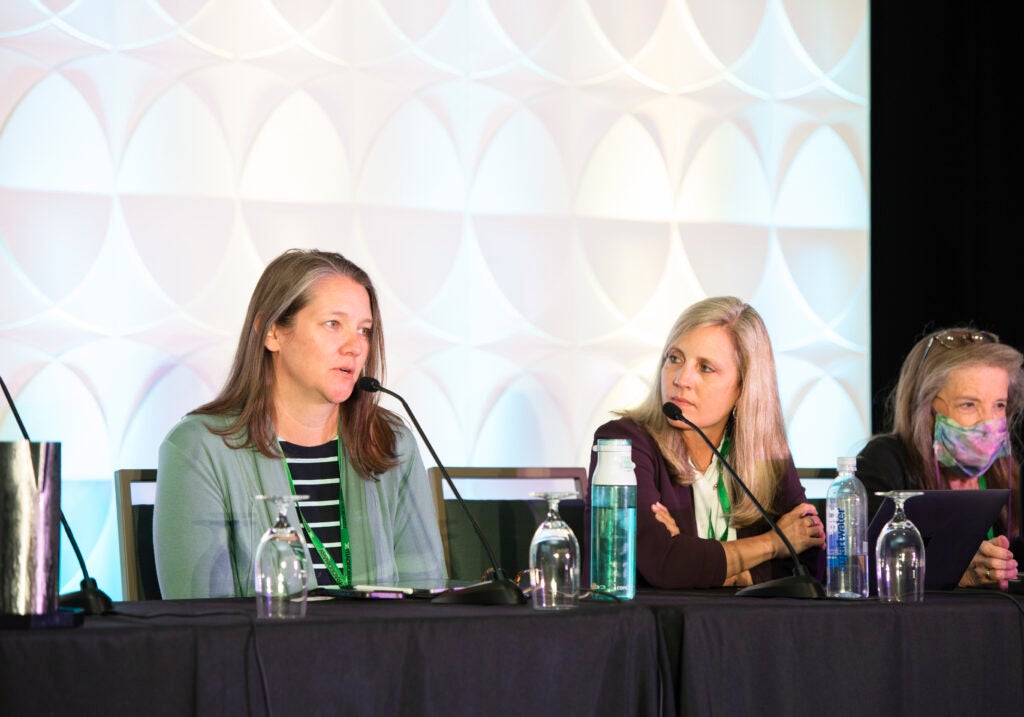 Three females sitting in front of microphones, one female is speaking while the other two listen.