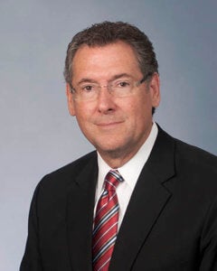 Gregg Harper while male wearing dark suite, white shirt, red tie.