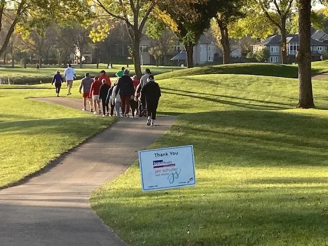 X Strides run/walk event and fundraiser participants walking on a sidewalk through a lovely park.