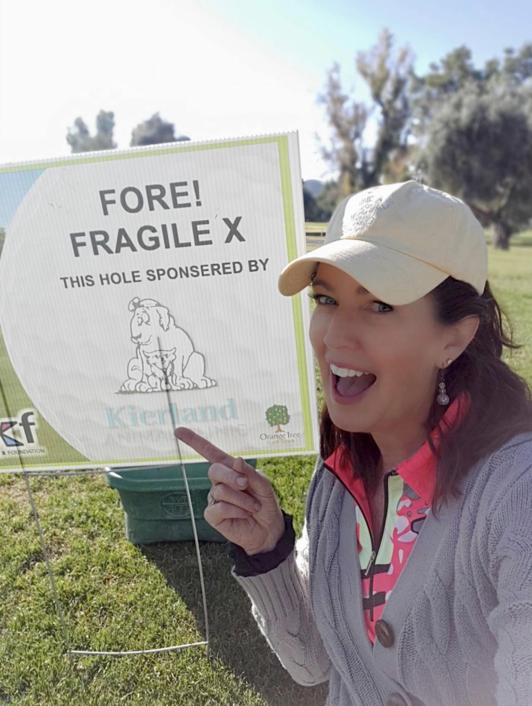 Golfer holds a sign saying FORE! Fragile X, this hole sponsored by Kierland Animal Clinic.