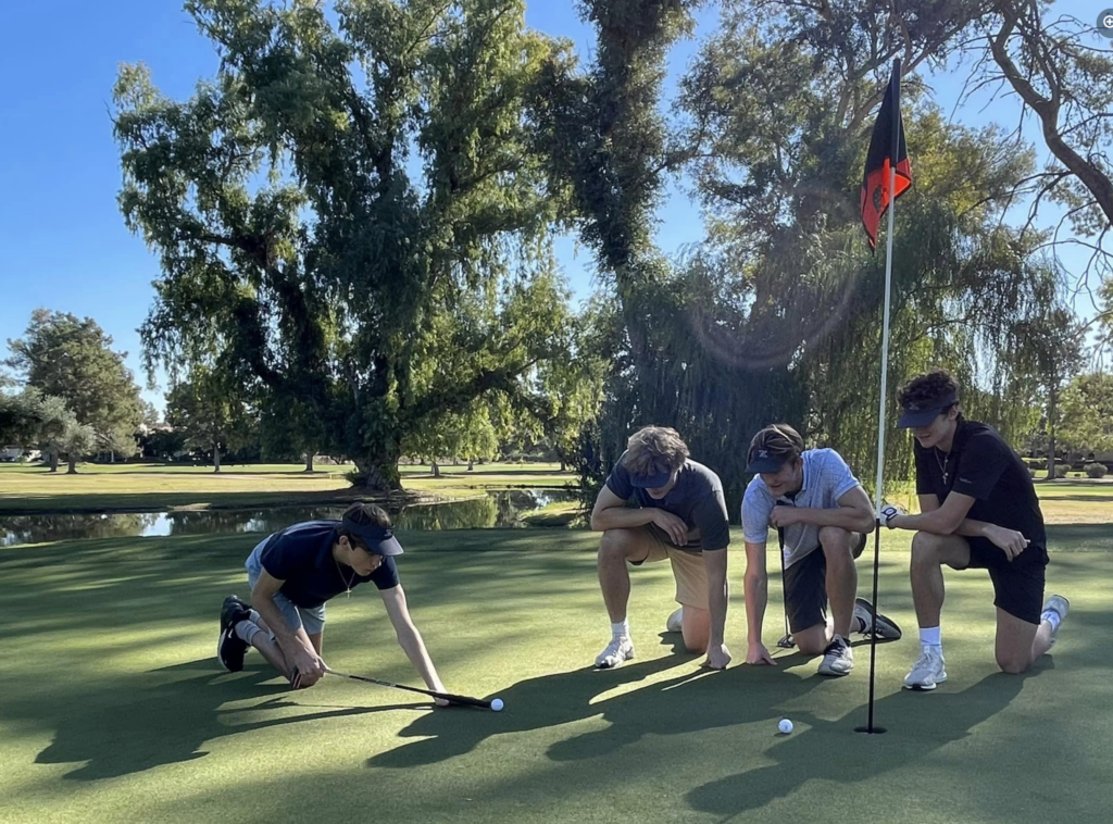four boys lining up their shot on the putting green