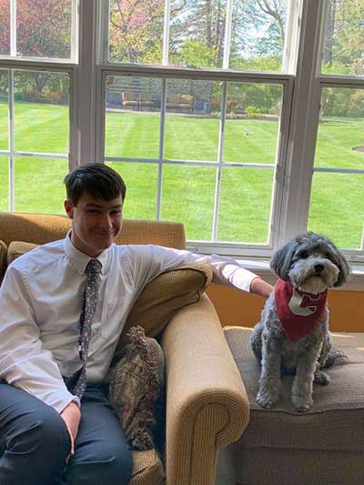 A young man, Andrew Frech, wearing a shirt and tie, sitting on a couch next to his dog.