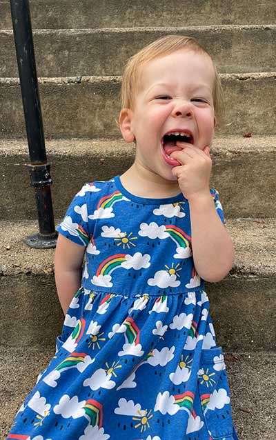 Annie Ruth wearing a dress covered in clouds and rainbows, having a big beautiful laugh. 