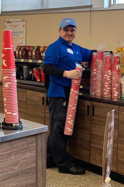 Austin Loeliger, an adult with Fragile X syndrome, at work wearing his uniform and sharing a huge smile.