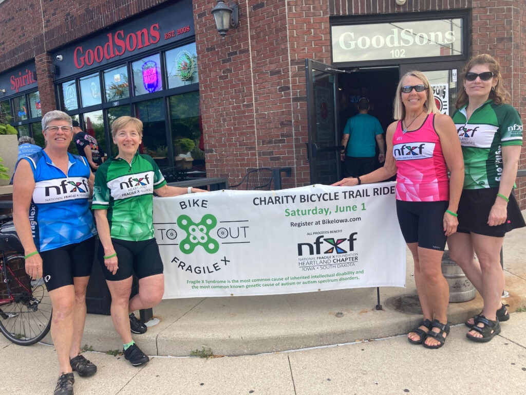 Nancy Carlson with 3 riders holding the event banner outside of GoodSons bar.