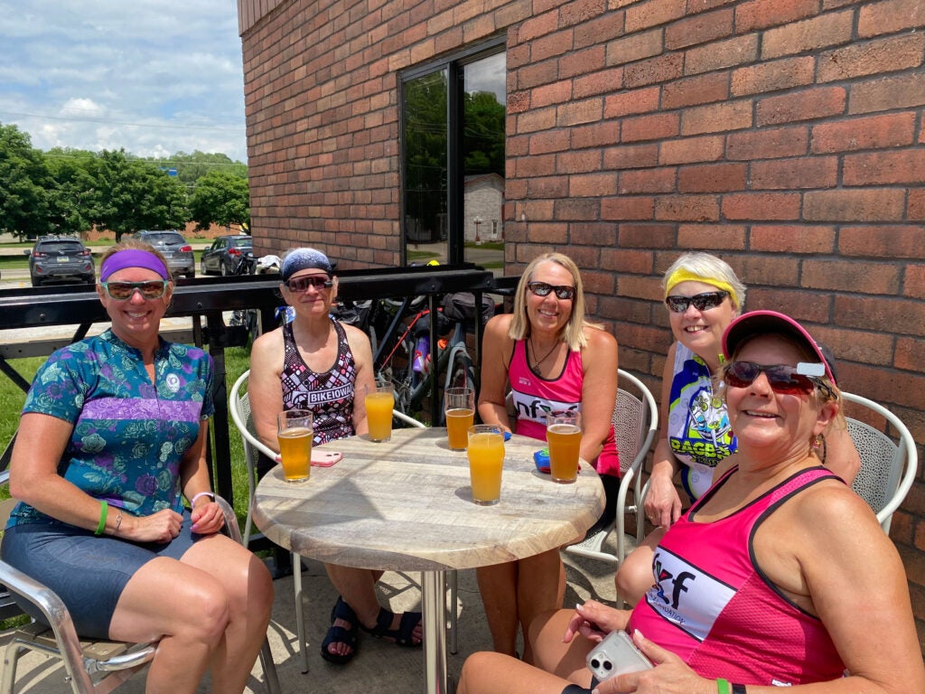 Nancy Carlson with 3 riders holding the event banner outside of GoodSons bar.