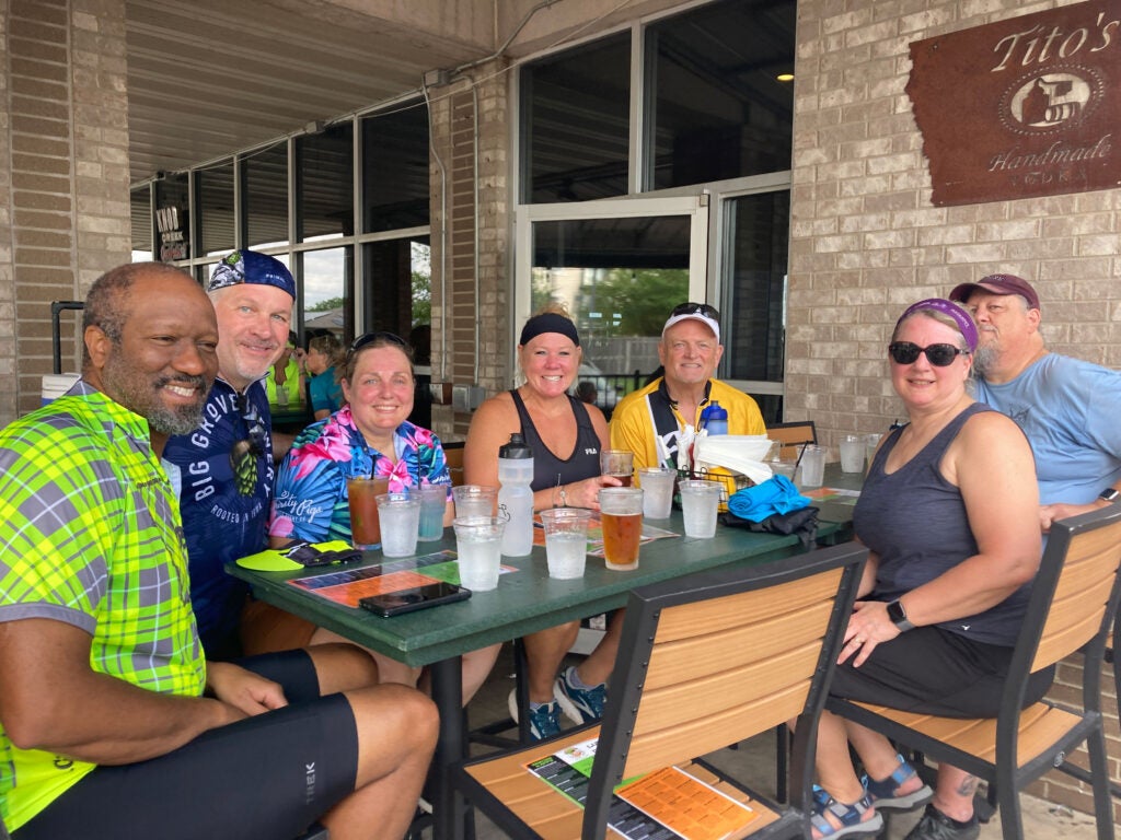 Nancy Carlson with 3 riders holding the event banner outside of GoodSons bar.