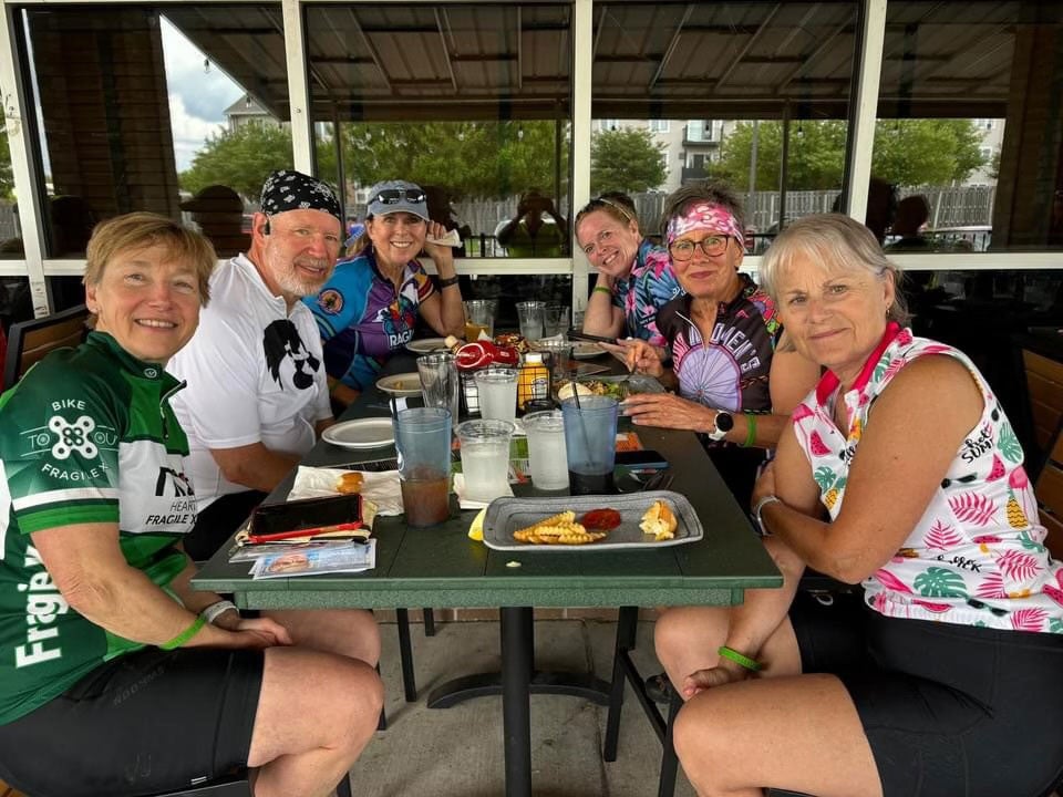 Nancy Carlson with 3 riders holding the event banner outside of GoodSons bar.