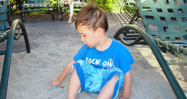 A young boy with Fragile X syndrome playing in a sandbox.