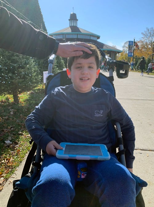 A young boy in a wheelchair with a computer tablet on his lap.