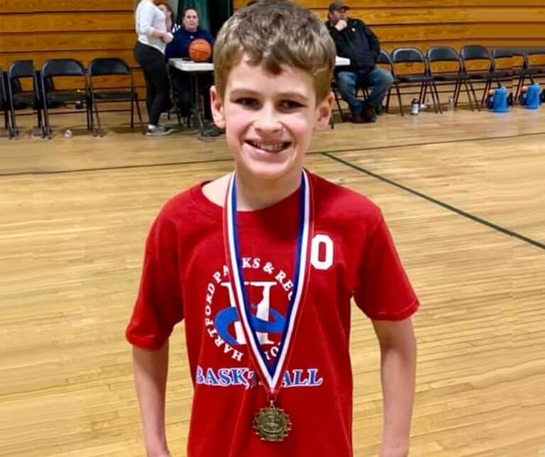 Brayden on a basketball court with a medal around his neck.