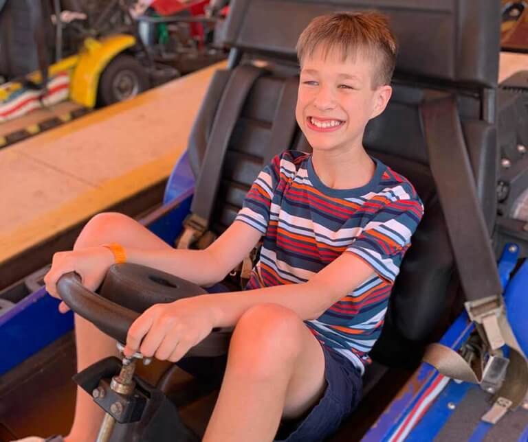 Brayden Crawford in a go cart, wearing shorts and a t-shirt, and a big smile.