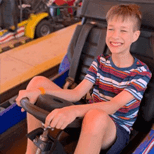 Young thin male riding an amusement park car wearing a t-shirt and shorts and smiling