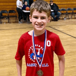 Young boy wearing a red t-shirt and a medal around his neck standing on an indoor basketball court