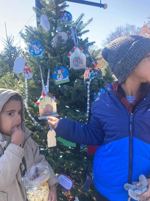 Two young boys, one eating popcorn, stand near their decorated Christmas tree.