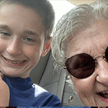 Young boy in a blue t-shirt and his grandmother with gray hair wearing sunglasses