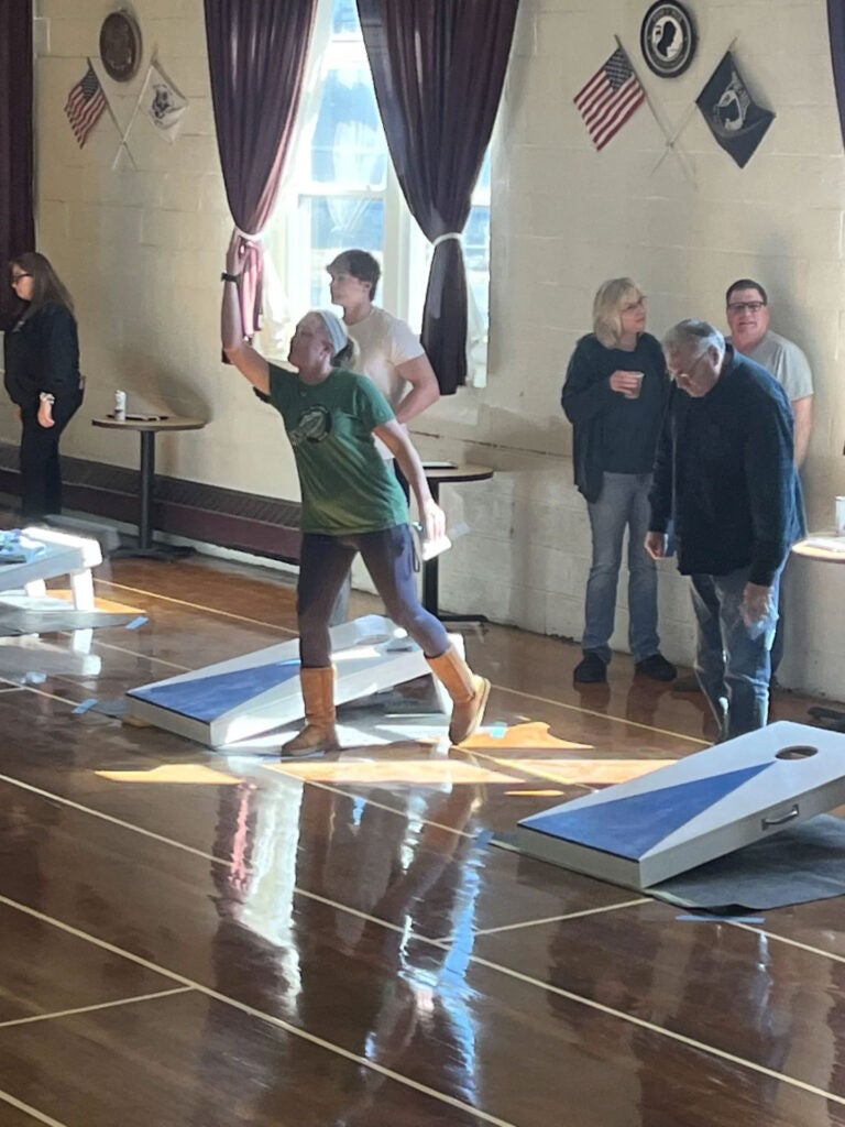 A woman tossing a bean bag in a corn hole contest in a gym.