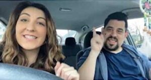 Danielle and Joey in a car, with Danielle driving and Joey showing Number 1 with his hand and finger.