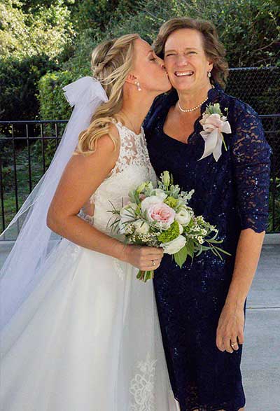 Kelley, in her wedding dress and holding a bouquet, kissing her mother Denise on the cheek.