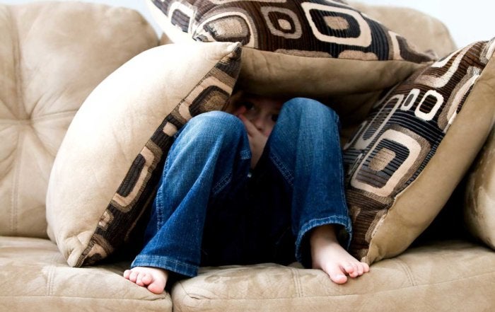 Boy hiding under cushions on a sofa