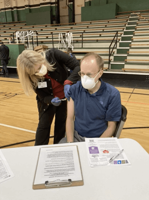 Dr. Erickson at a gymnasium in Indiana receiving his first COVID-19 vaccination from a nurse.