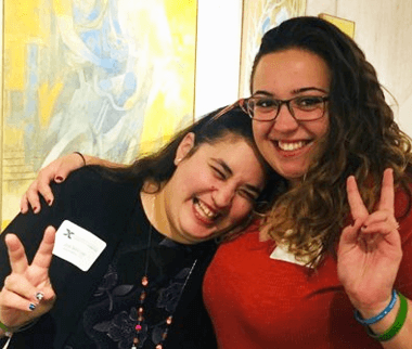 Two females holding up their hands in a peace sign, one with her arm around the other