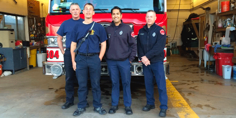 Ian with three members of the local fire station standing in front of a fire truck.